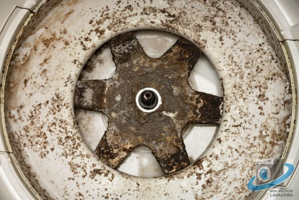 Uma visão de perto do interior de uma máquina de lavar suja, com acúmulo de sujeira e mofo no agitador. A imagem ilustra como os resíduos podem danificar os componentes internos do aparelho